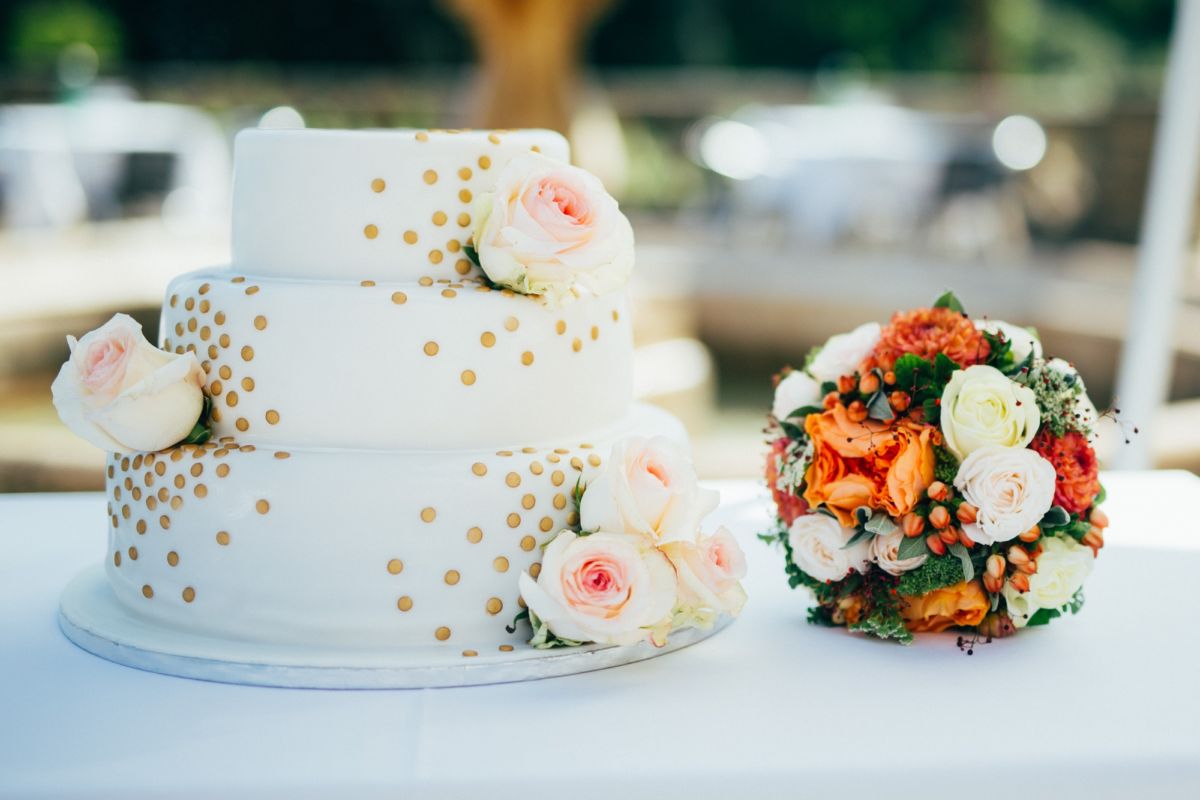 Dreistöckige Hochzeitstorte mit goldenen Pünktchen und frischen Rosen