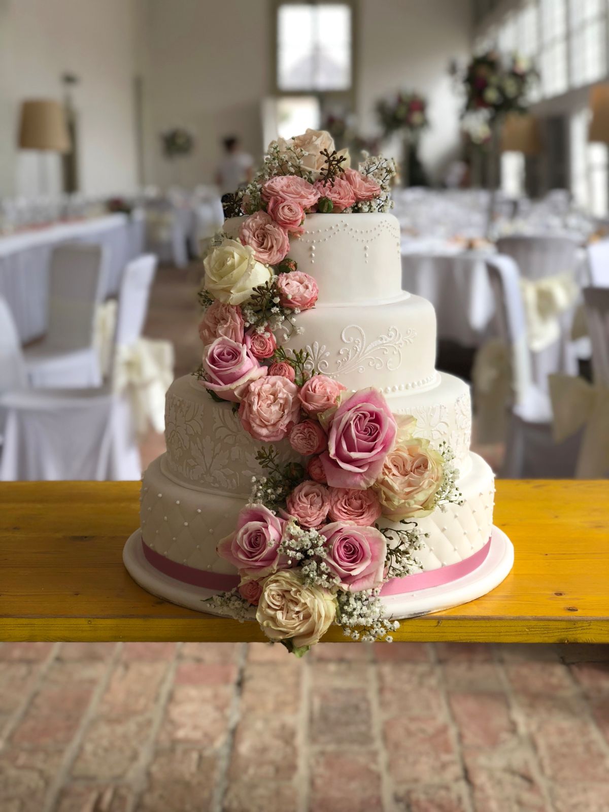 Vierstöckige Hochzeitstorte mit Perlendekor und rosa Rosenkaskade