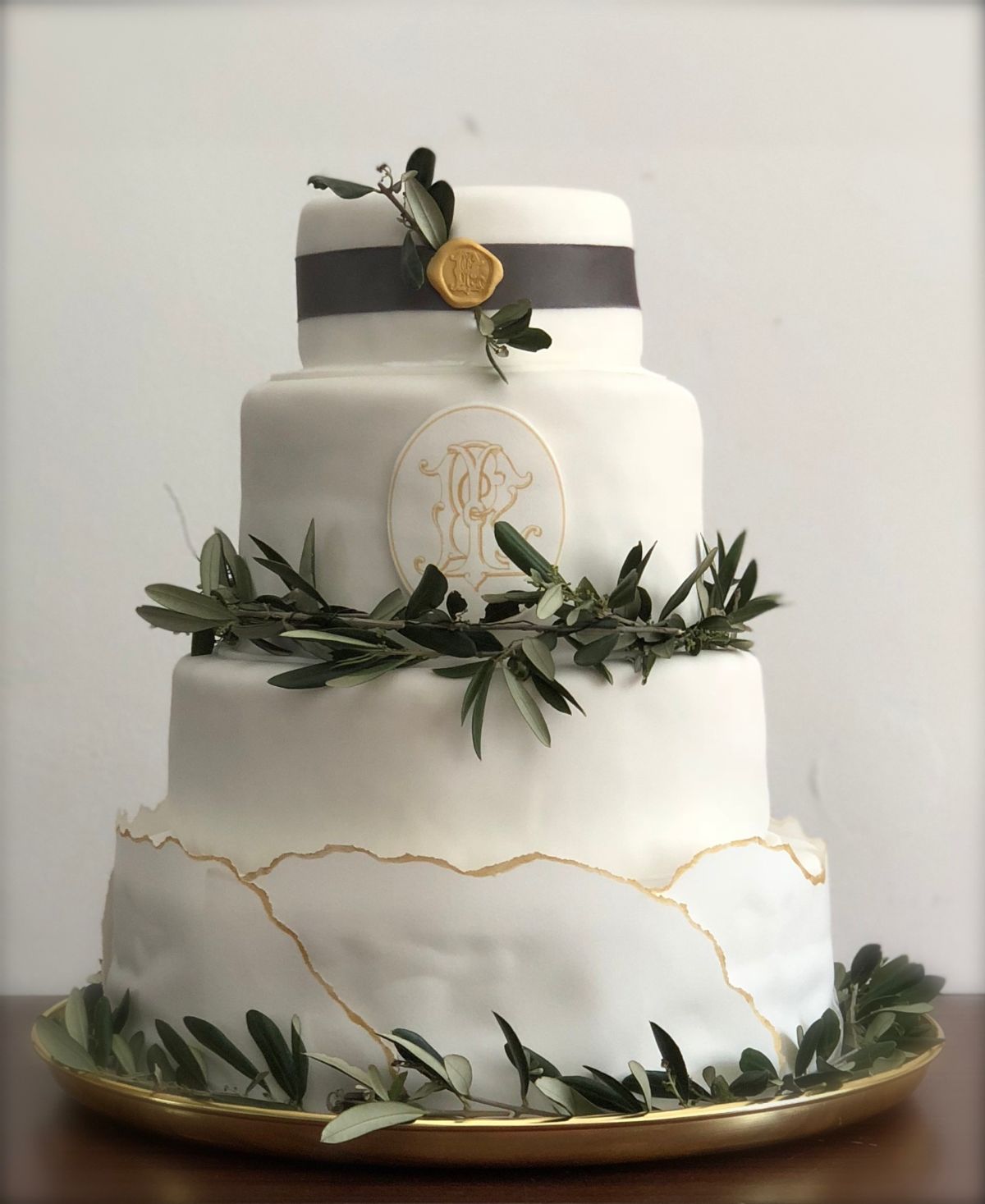 Vierstöckige Hochzeitstorte in Weiß mit schwarzem Band, Goldrose und Olivenlaub auf Goldständer