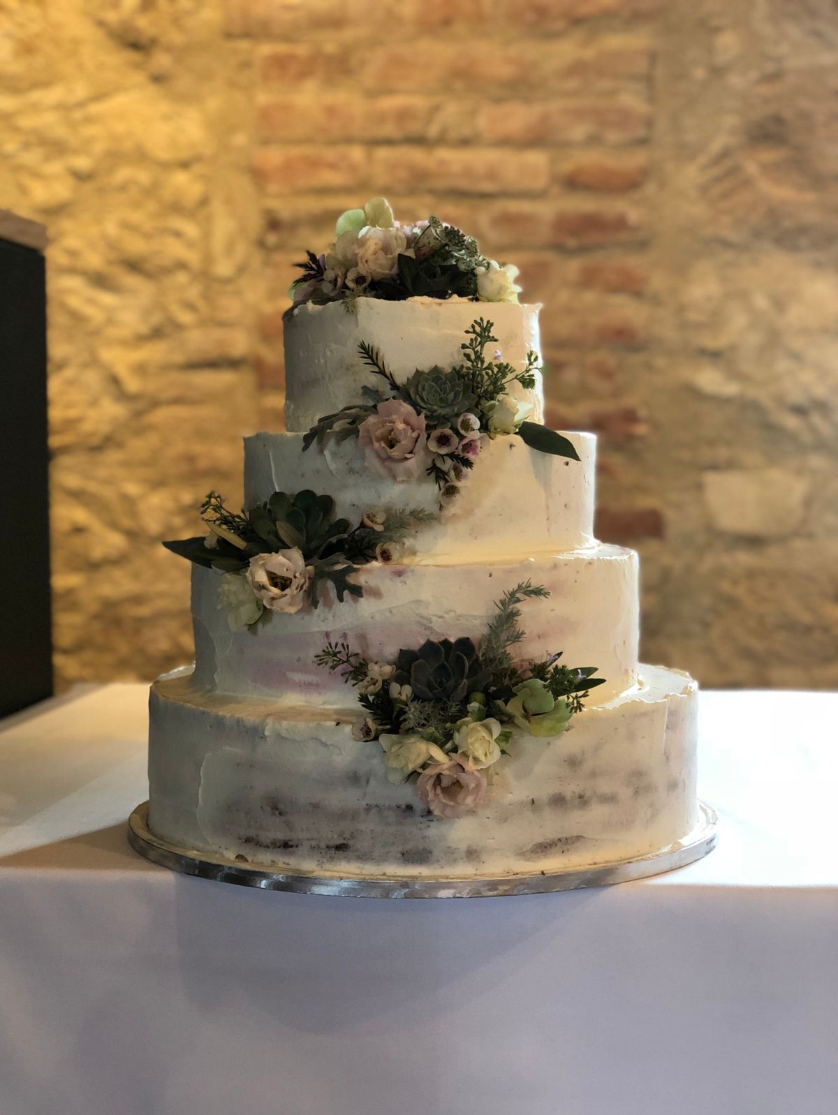 Vierstöckige Hochzeitstorte halbgedeckt mit dramatischer Blütenkaskade und dunklen Federn