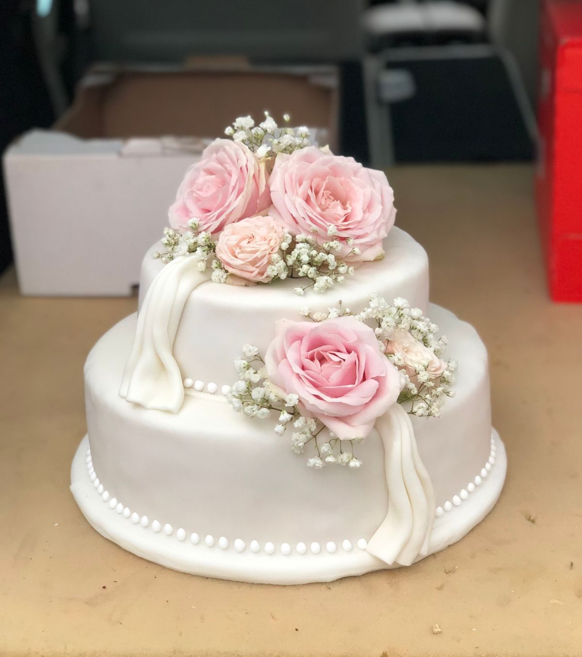 Zweistöckige Hochzeitstorte mit weißen Seidentüchern, rosa Rosen und Perlenkranz