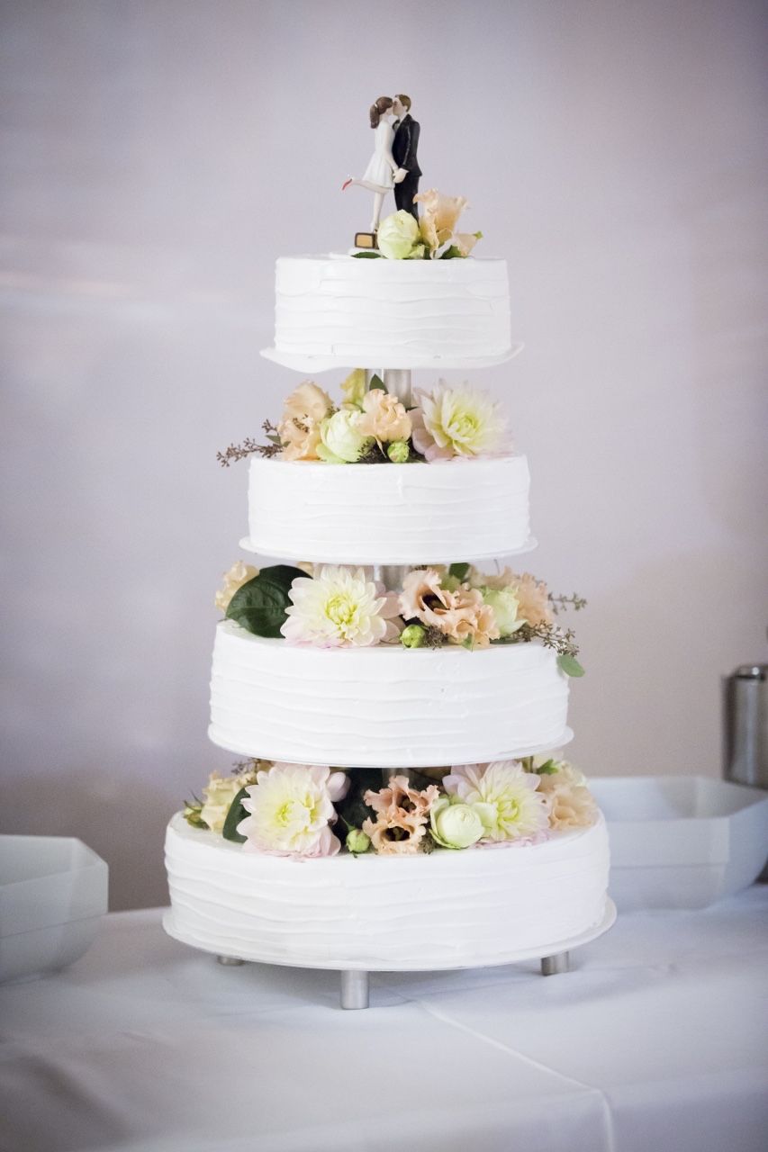 Vierstöckige Hochzeitstorte mit Brautpaar-Figur und bunten frischen Blüten