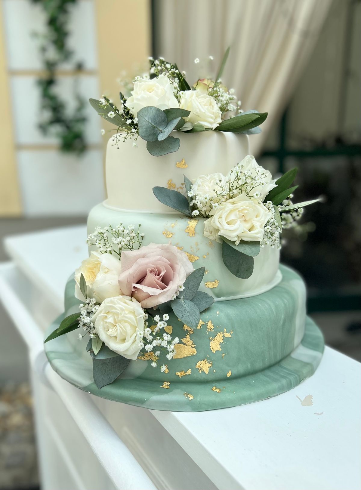 Dreistöckige Hochzeitstorte in Salbeigrün und Weiß mit Blattgold, weißen Rosen und Eukalyptus