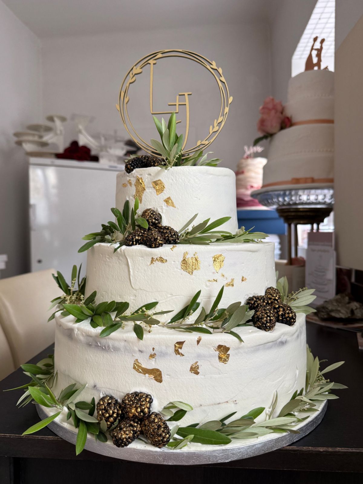Dreistöckige Hochzeitstorte mit Blattgold, Olivenzweigen, vergoldeten Brombeeren und Monogramm-Topper
