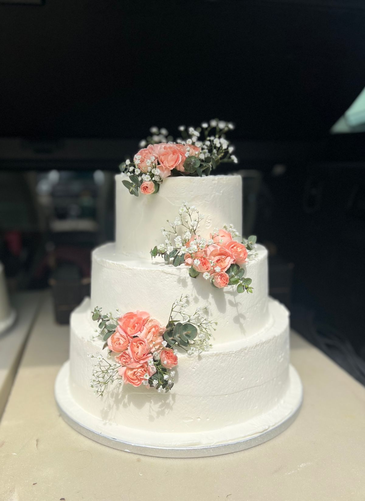 Dreistöckige Hochzeitstorte in Weiß mit korallfarbenen Rosen, Schleierkraut und Eukalyptus