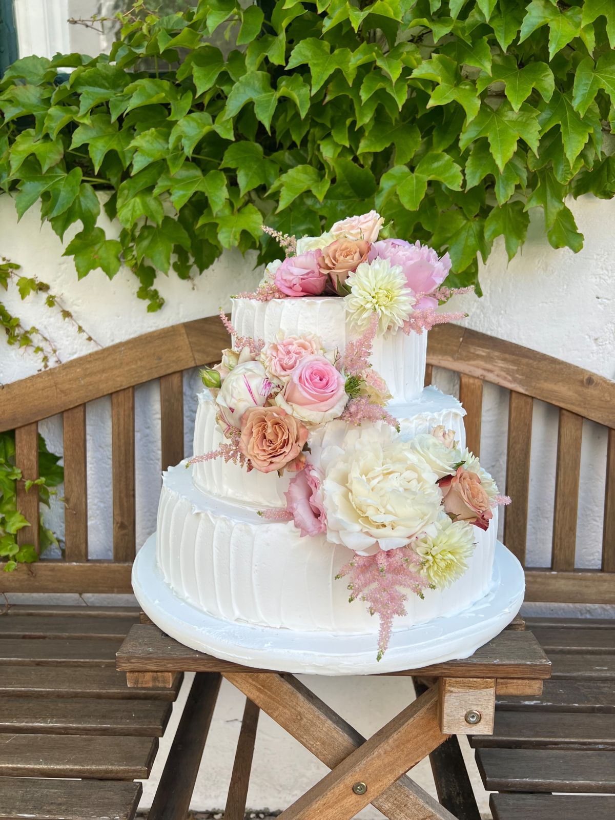 Zweistöckige Hochzeitstorte mit Rillenstruktur, Rosen und Dahlien auf einer Gartenbank