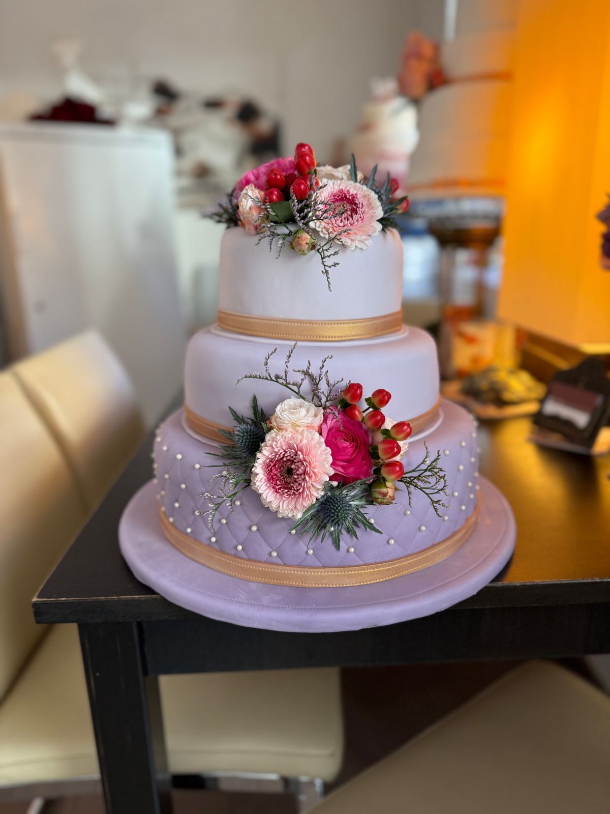 Dreistöckige Hochzeitstorte in Flieder mit Goldband, Zuckerperlen, Gerbera und Rosen