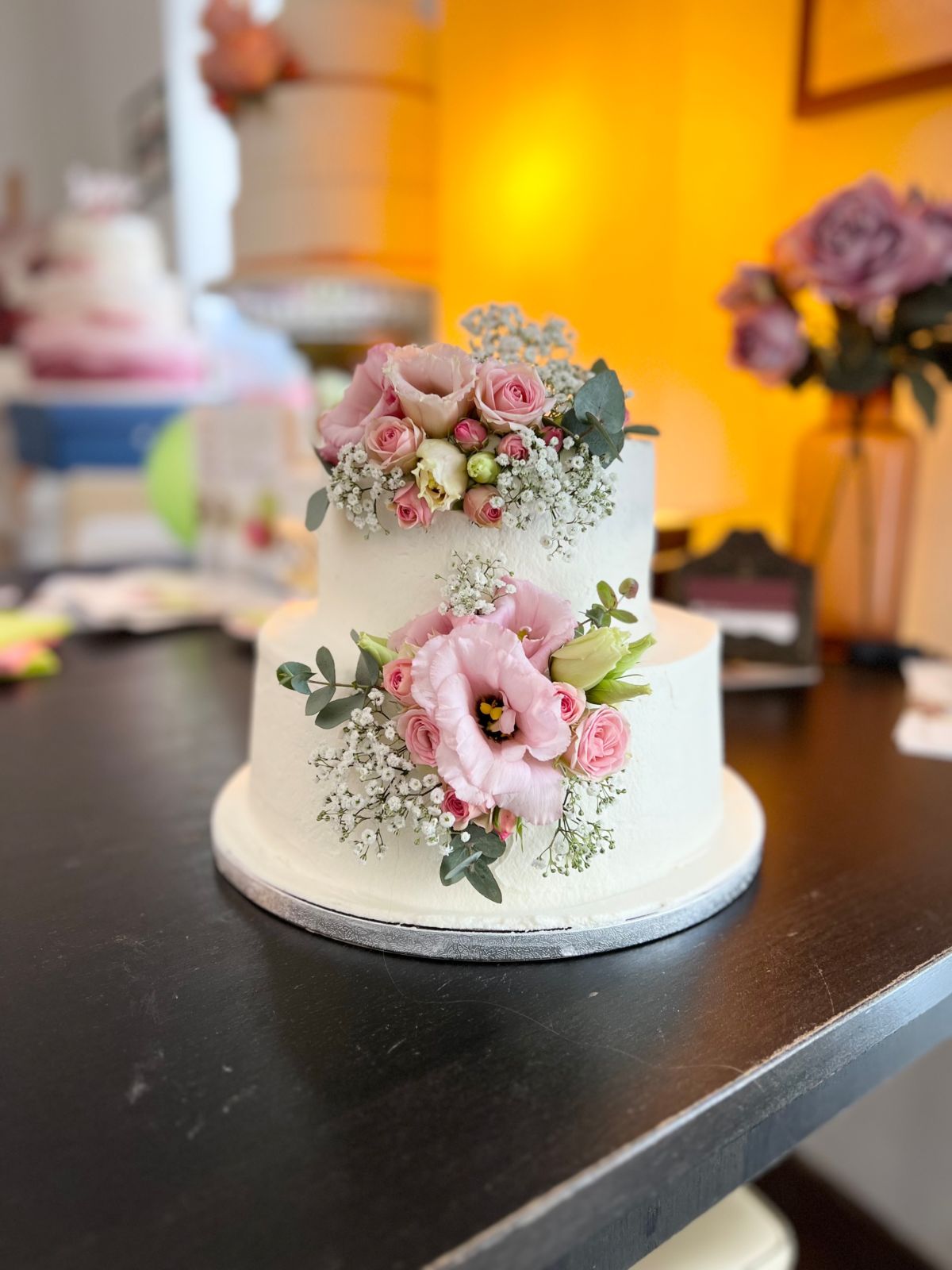 Zweistöckige Hochzeitstorte in Weiß mit rosa Lisianthus, Rosen und Schleierkraut