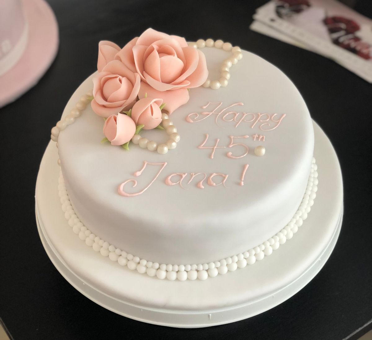 Einstöckige Torte mit weißem Fondant, rosa Zuckerblüten und Perlenrand