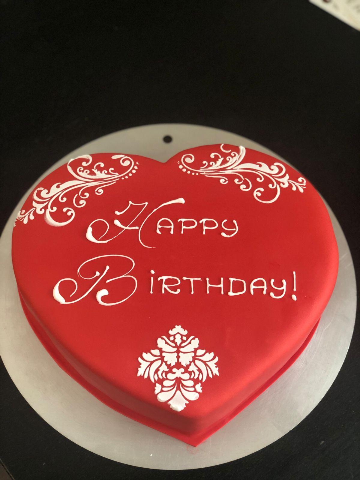 Herzförmige Torte in Rot mit weißem Schriftzug und Ornamentdekor