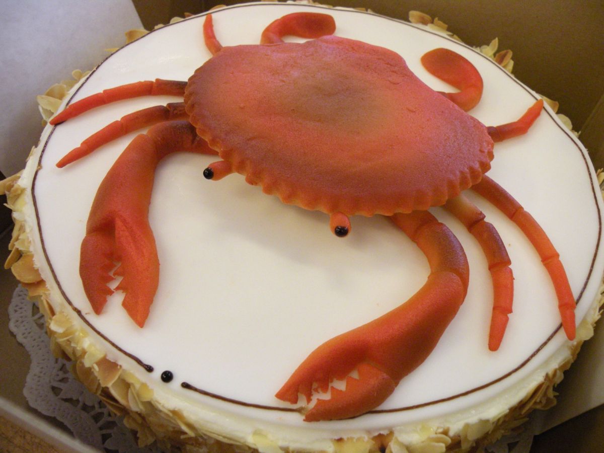 Motivtorte mit großer, rot modellierter Krabbe auf weißer Grundlage
