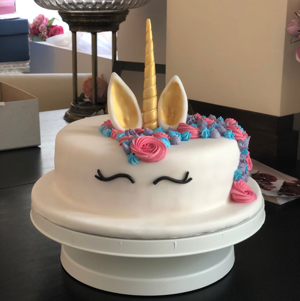 Kindergeburtstagstorte als Einhorn mit weißem Fondant, goldenem Horn und Zuckerblüten in Rosa und Türkis