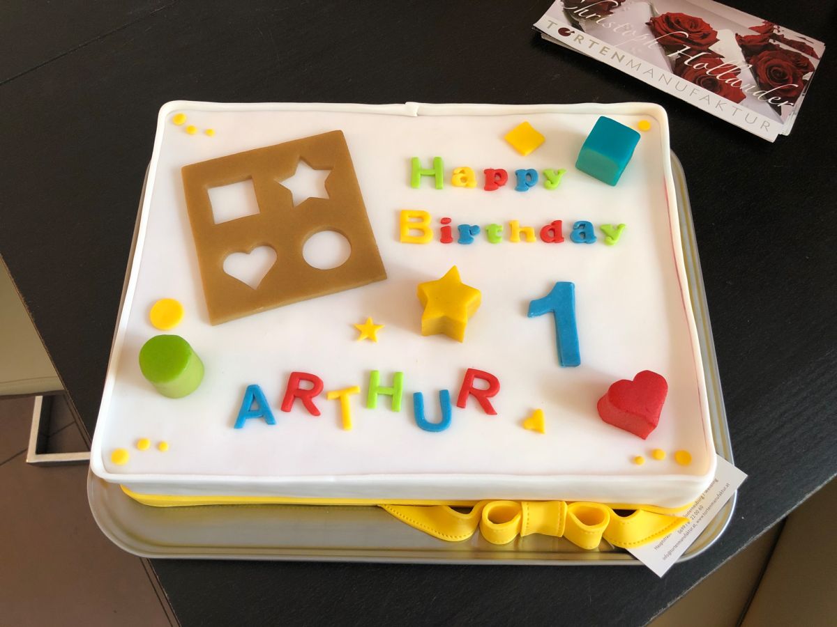 Kindergeburtstagstorte mit bunten Spiel-Formen, Zahlen, Namen und Happy-Birthday-Schriftzug auf weißem Fondant