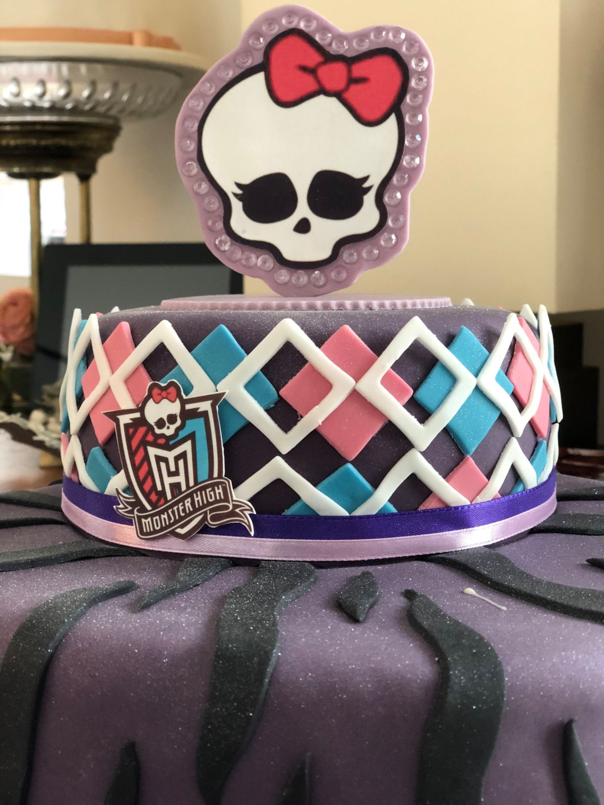 Zweistöckige Monster-High-Torte mit lila Tigerstreifen, buntem Rautenmuster und großem Totenkopf-Aufsatz