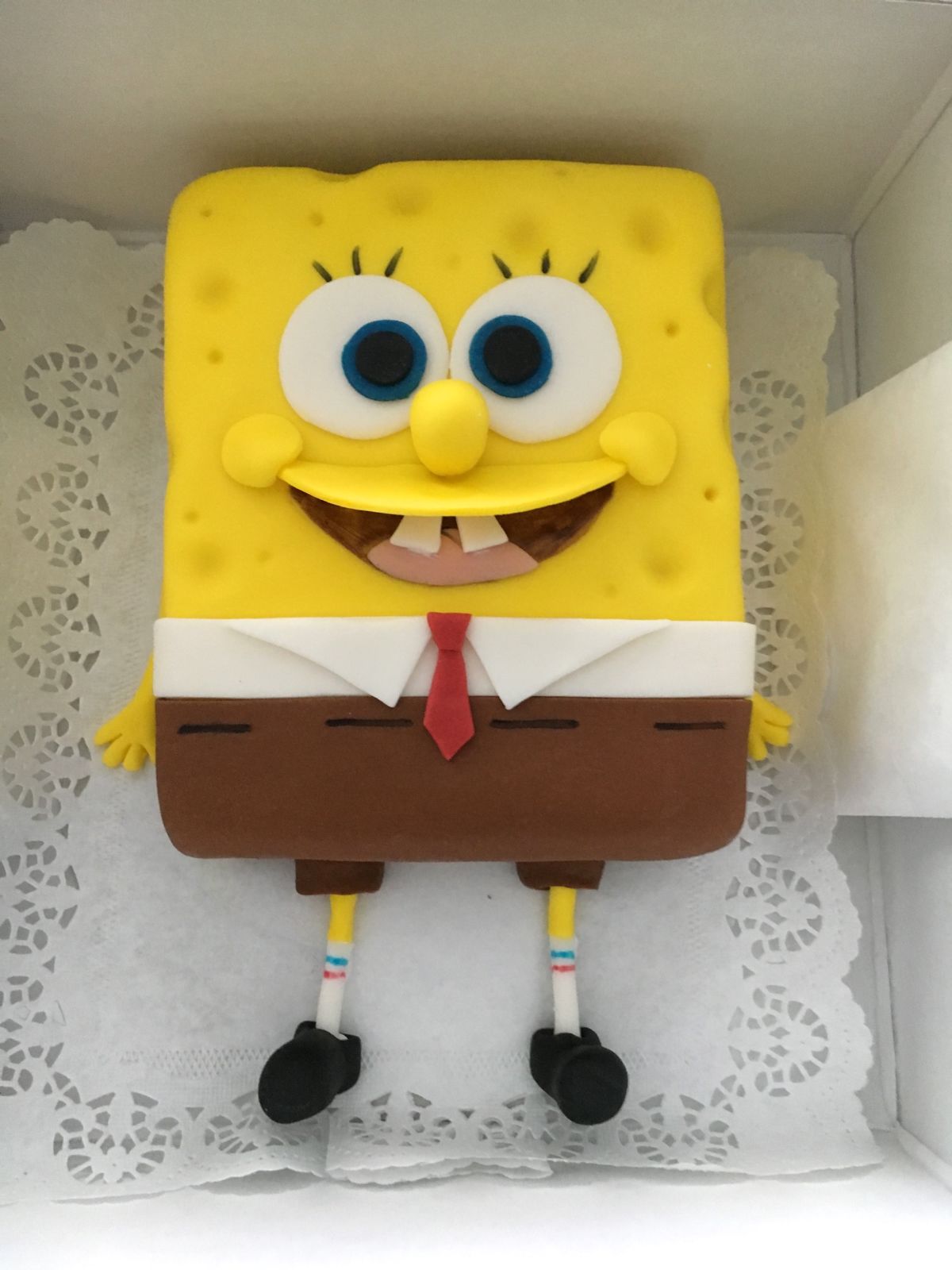Kindergeburtstagstorte als SpongeBob mit gelbem Fondant, großen blauen Augen und brauner Hose mit roter Krawatte