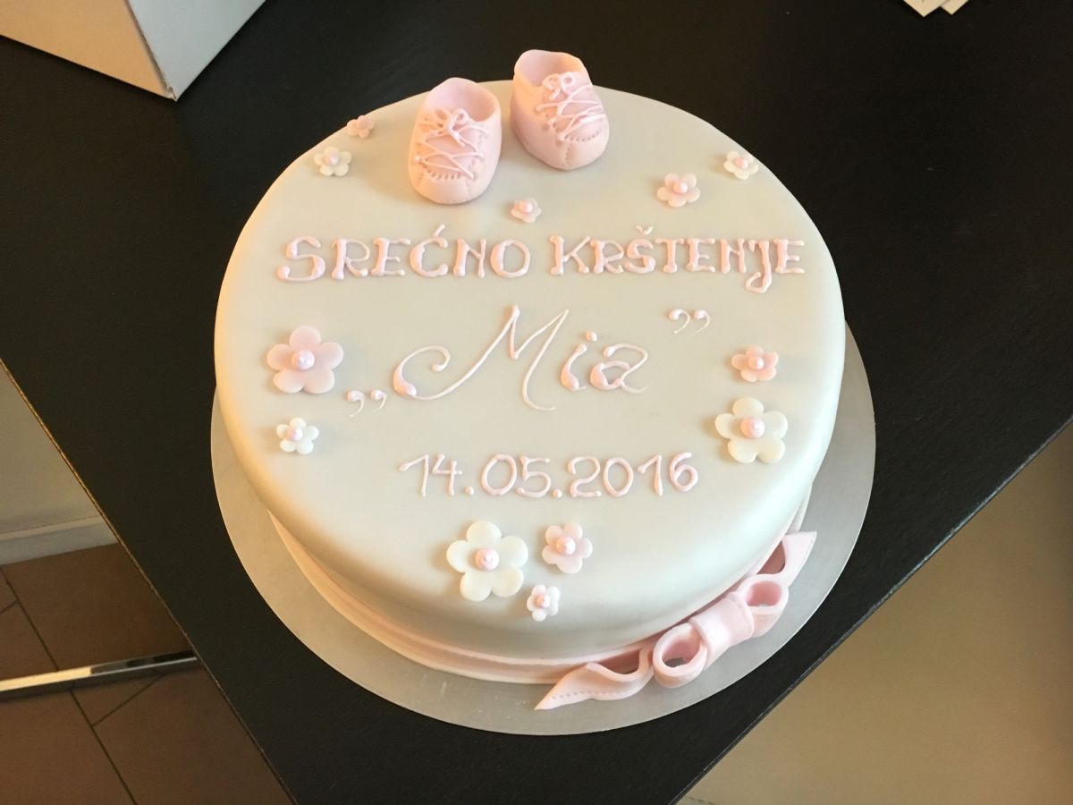 Tauftorte mit rosa Babyschuhen oben und verteilten Zuckerblümchen
