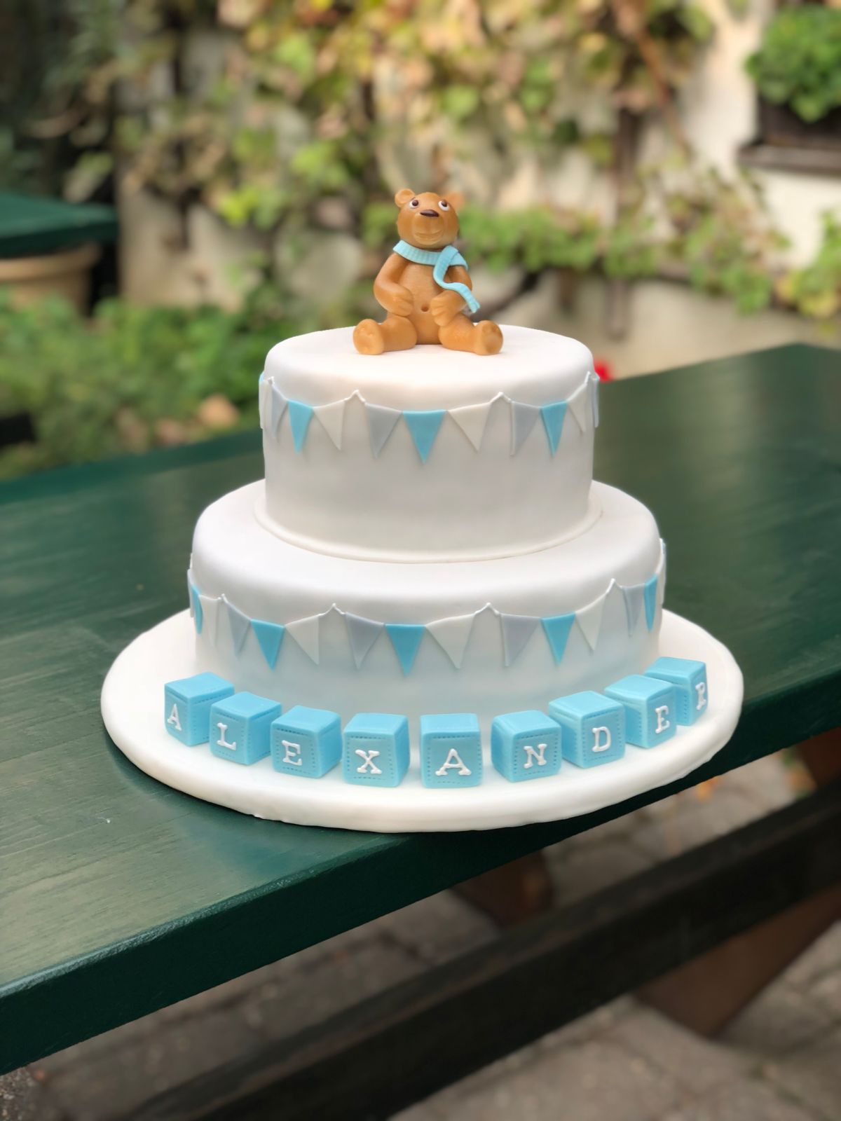 Zweistöckige Tauftorte mit Teddybär im Schal und Wimpelkette