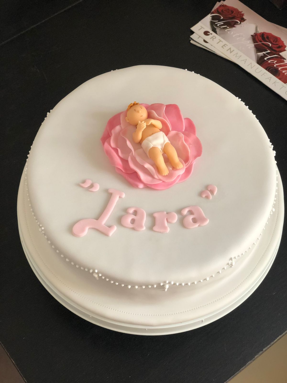 Weiße Tauftorte mit Fondant-Engel auf rosa Blütenbett