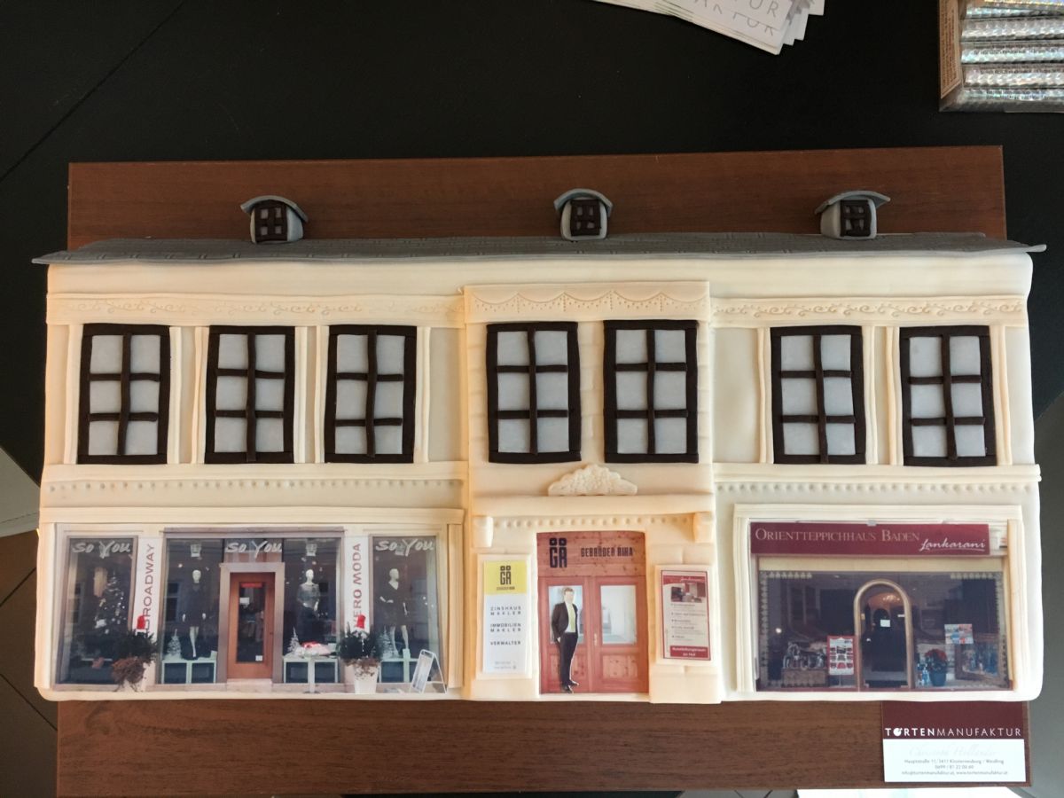 Architektur-Motivtorte einer dreistöckigen Einkaufsstraße mit cremefarbenem Fondant und Schaufenstern