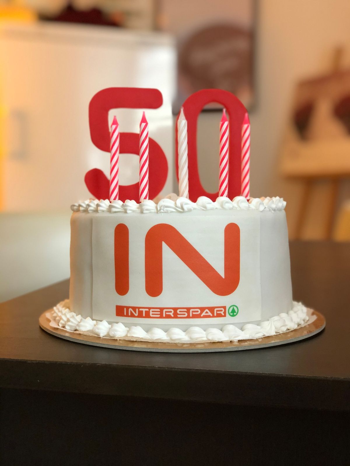 Runde Firmentorte zum 50-jährigen Interspar-Jubiläum mit weißem Fondant, roten Zahlen und Logo