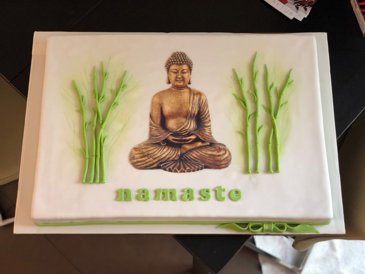 Rechteckige Torte in Weiß mit Buddha-Motiv, Bambusstängeln links und rechts, grüner Text „namaste“
