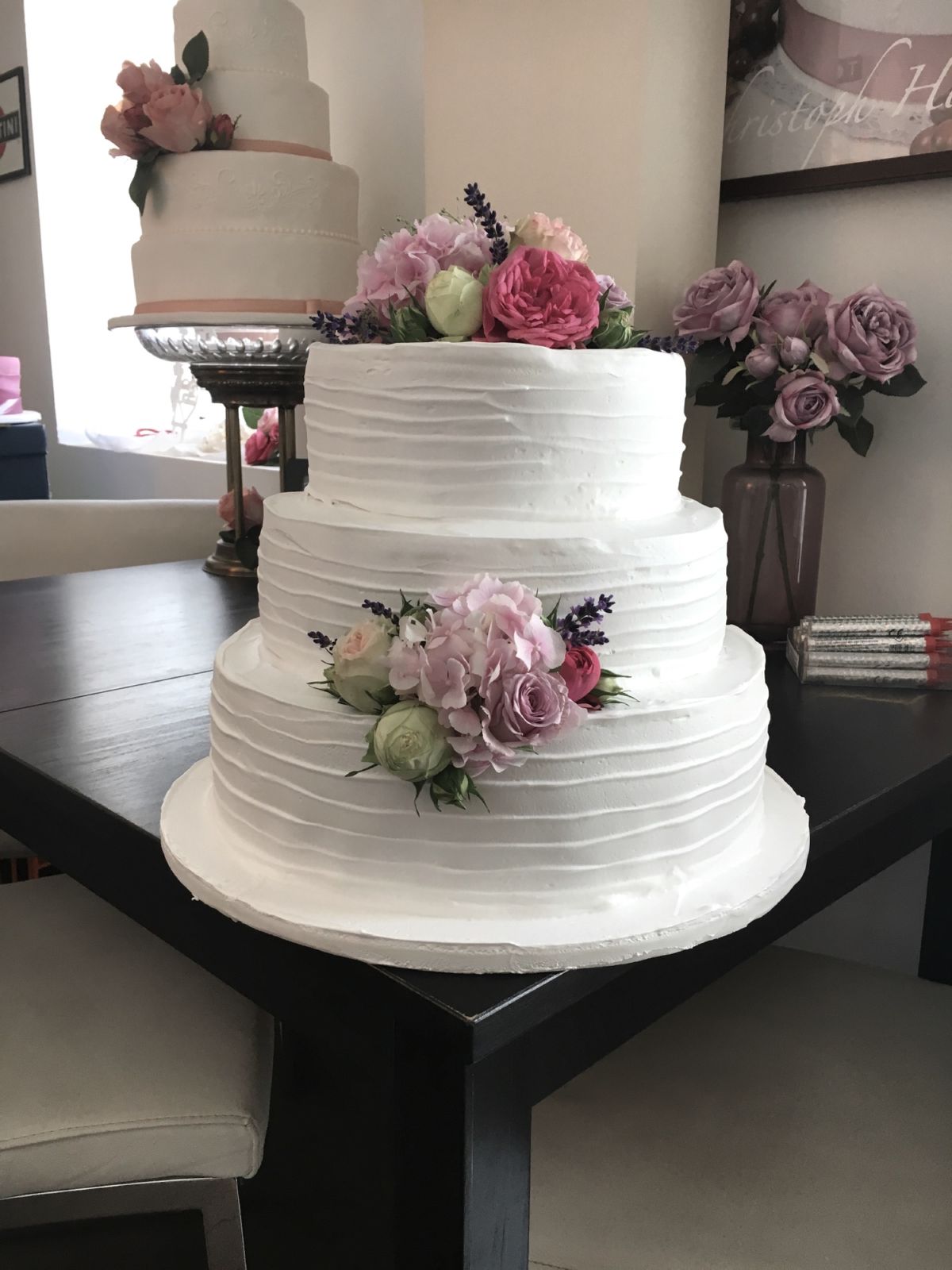 Three-tier white wedding cake with decorative pattern and pink and mauve roses