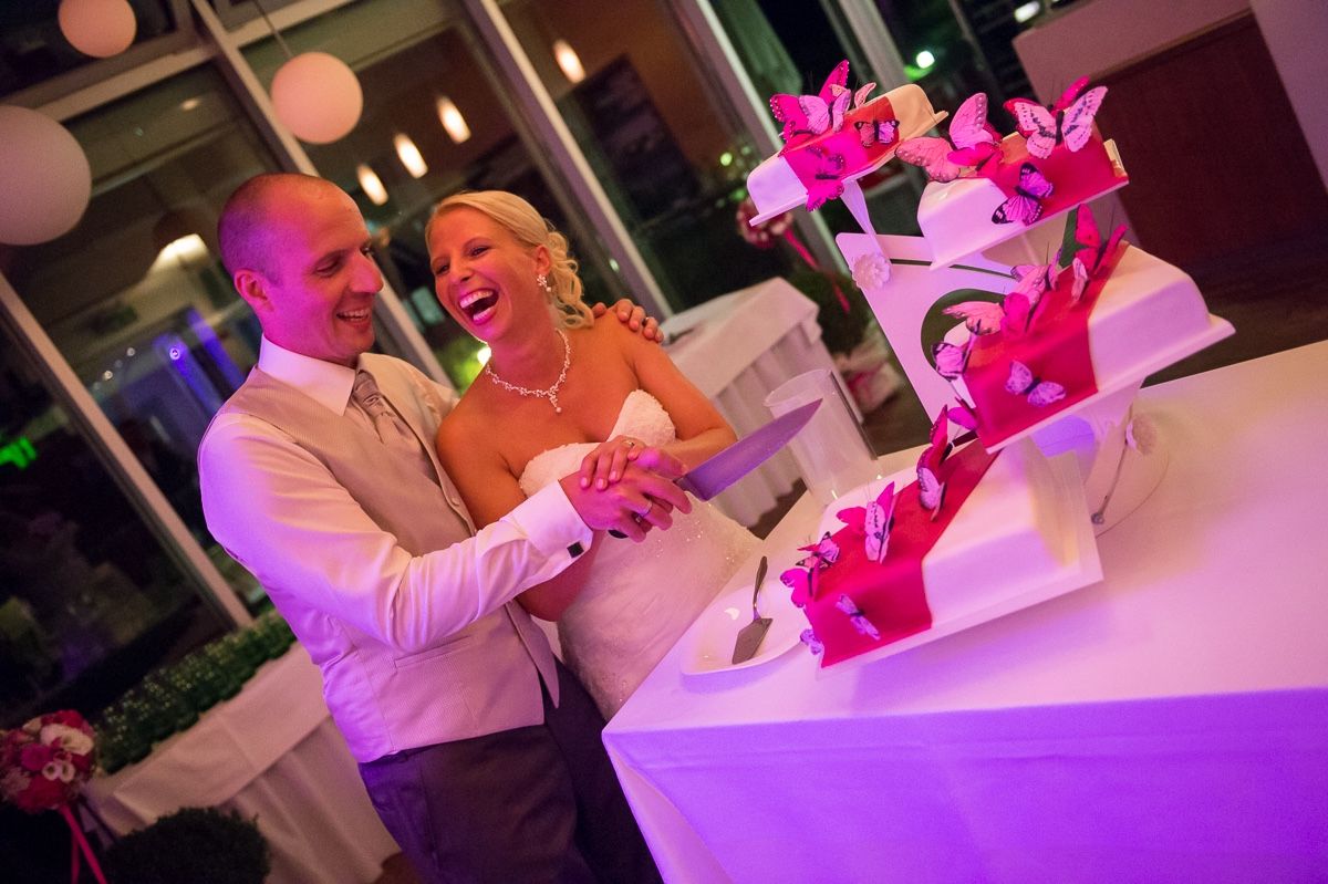 Bride and groom cutting tiered wedding cake with pink and white layers