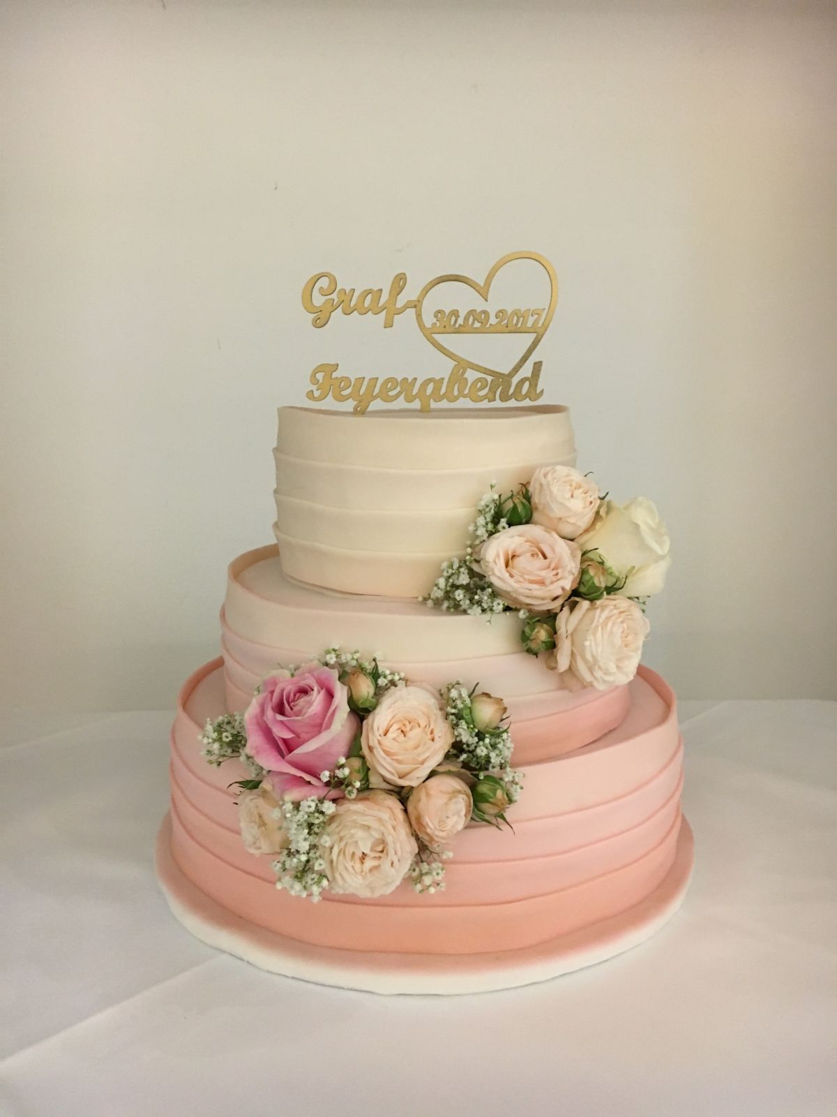 Three-tier white wedding cake with gold name topper and pastel rose decoration