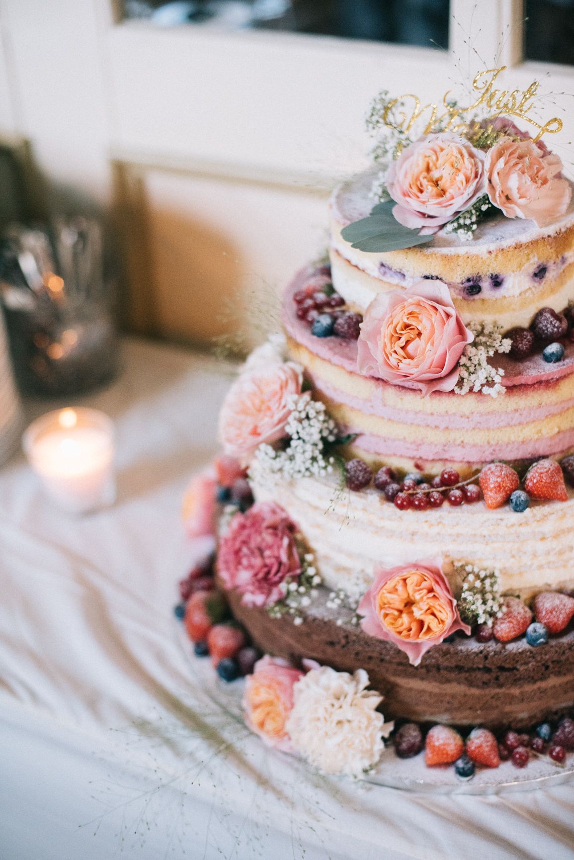 Four-tier naked cake with visible layers in brown and pink with fresh berries