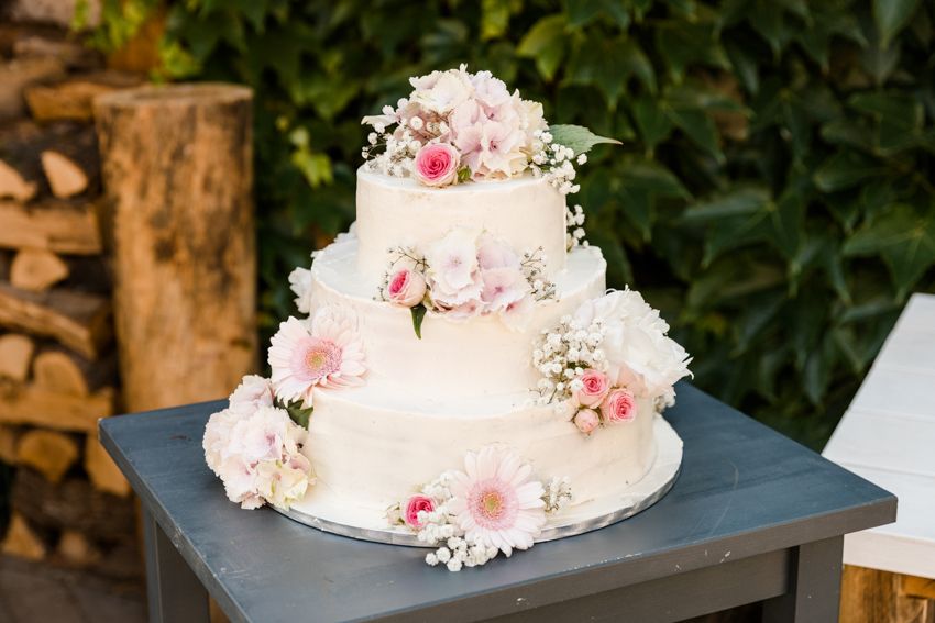 Three-tier white wedding cake with fresh pink dahlias and baby’s breath outdoors