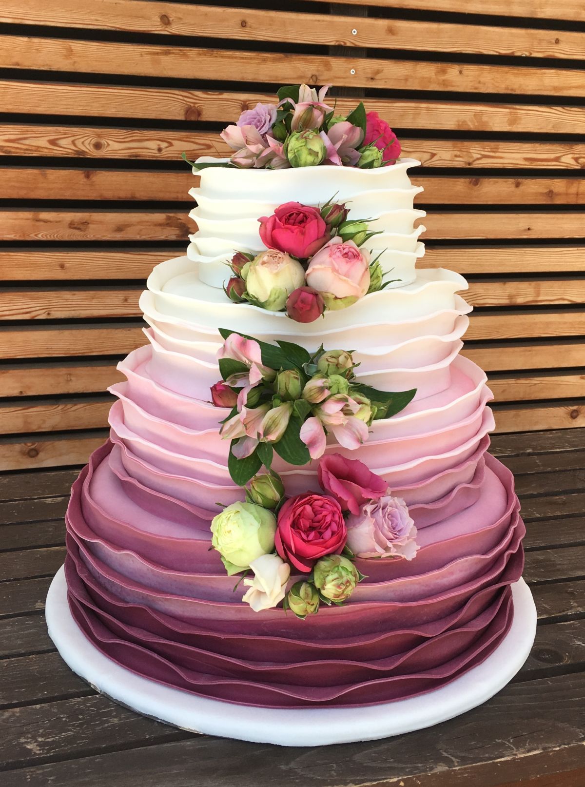 Four-tier ombré wedding cake fading from white to burgundy with fresh roses