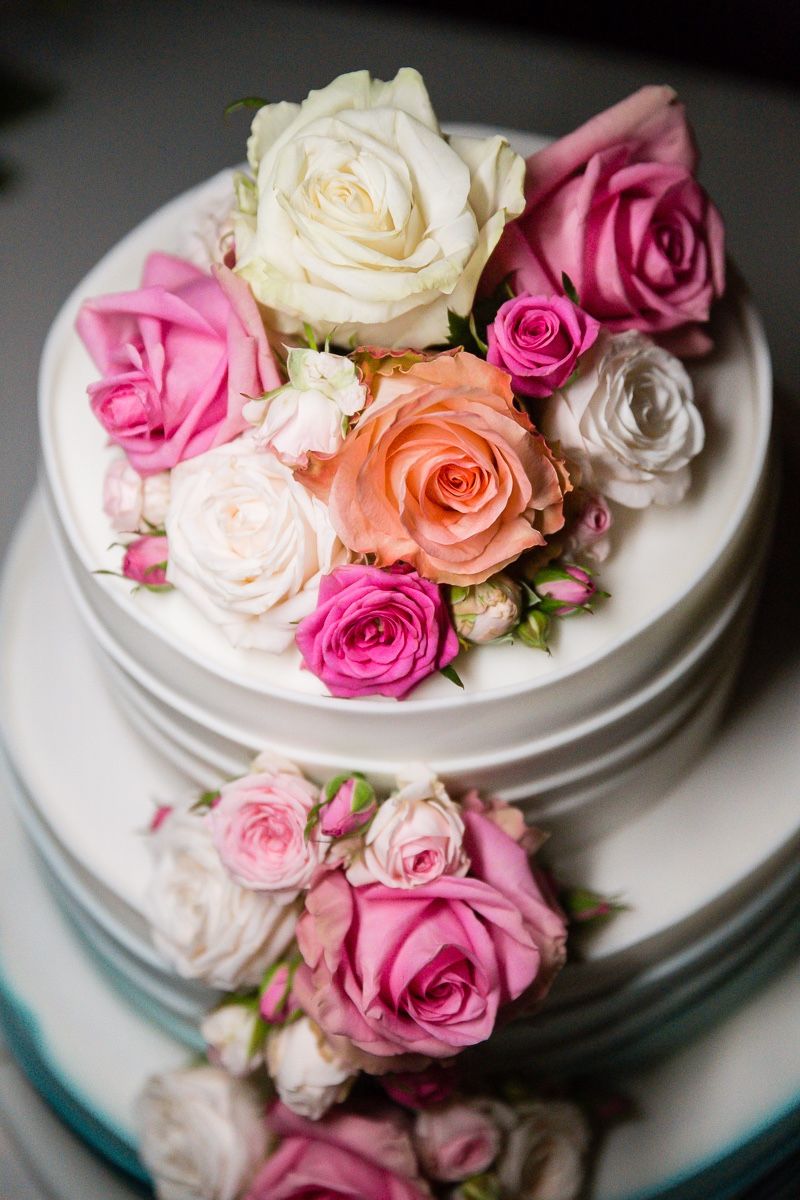 Two-tier white wedding cake with cascading arrangement of pastel-shade roses