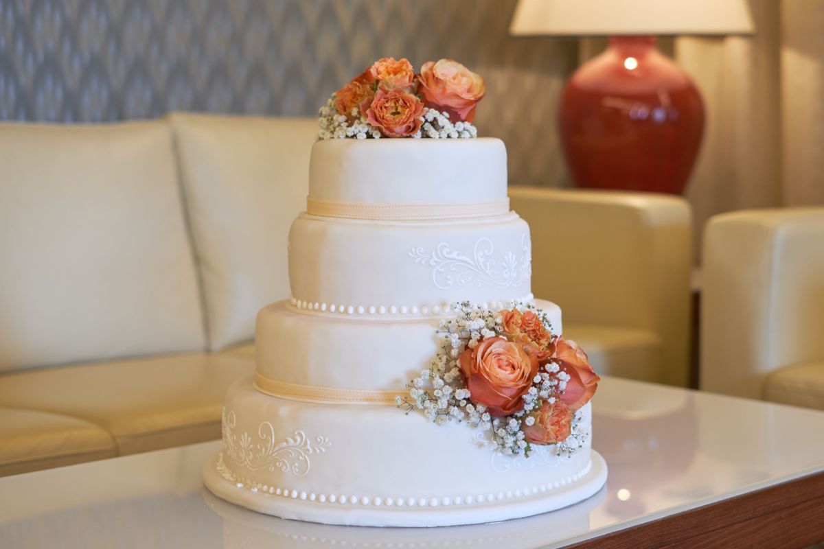 Four-tier white wedding cake with apricot roses and silk ribbons between tiers