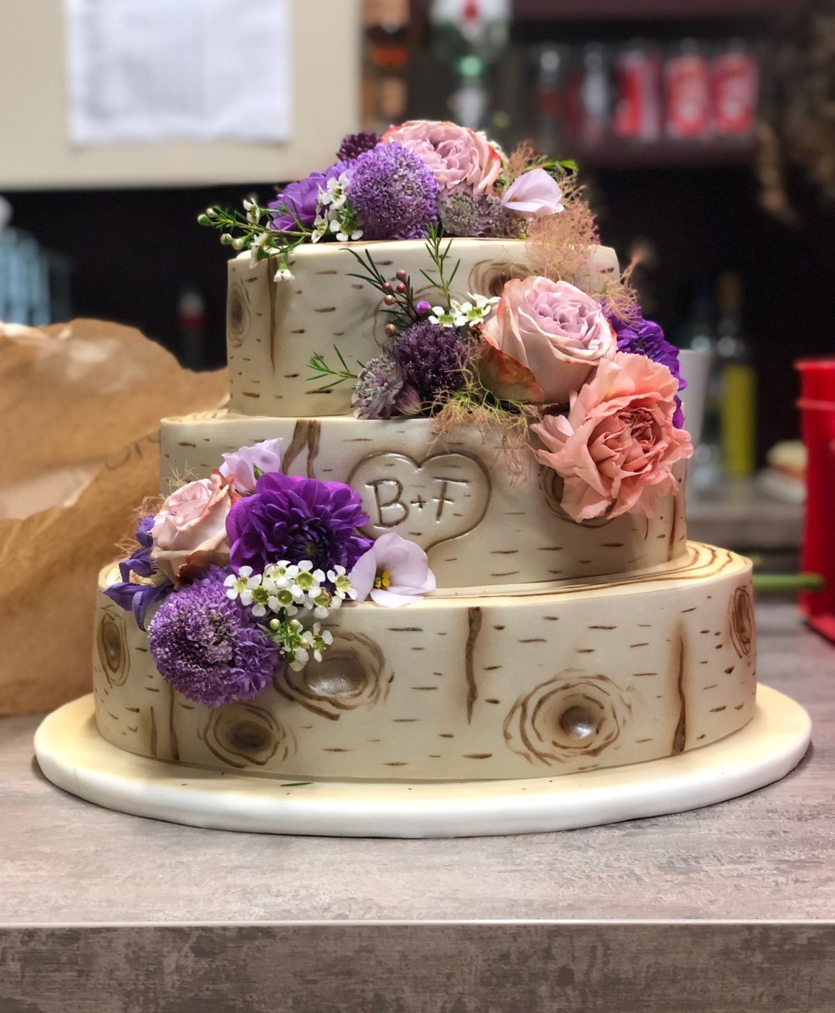 Three-tier birch-bark textured cake with a heart monogram and mauve and pink florals