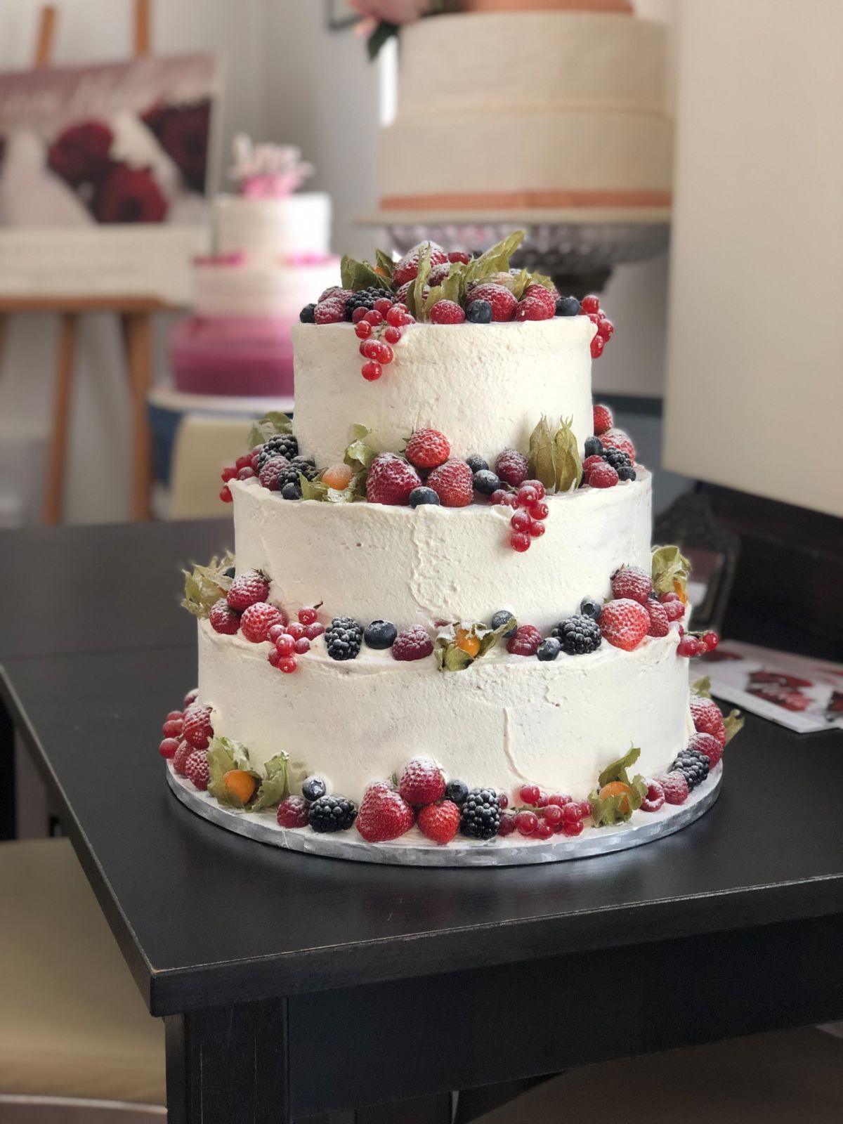 Three-tier wedding cake with textured frosting decorated with raspberries, blackberries and red currants