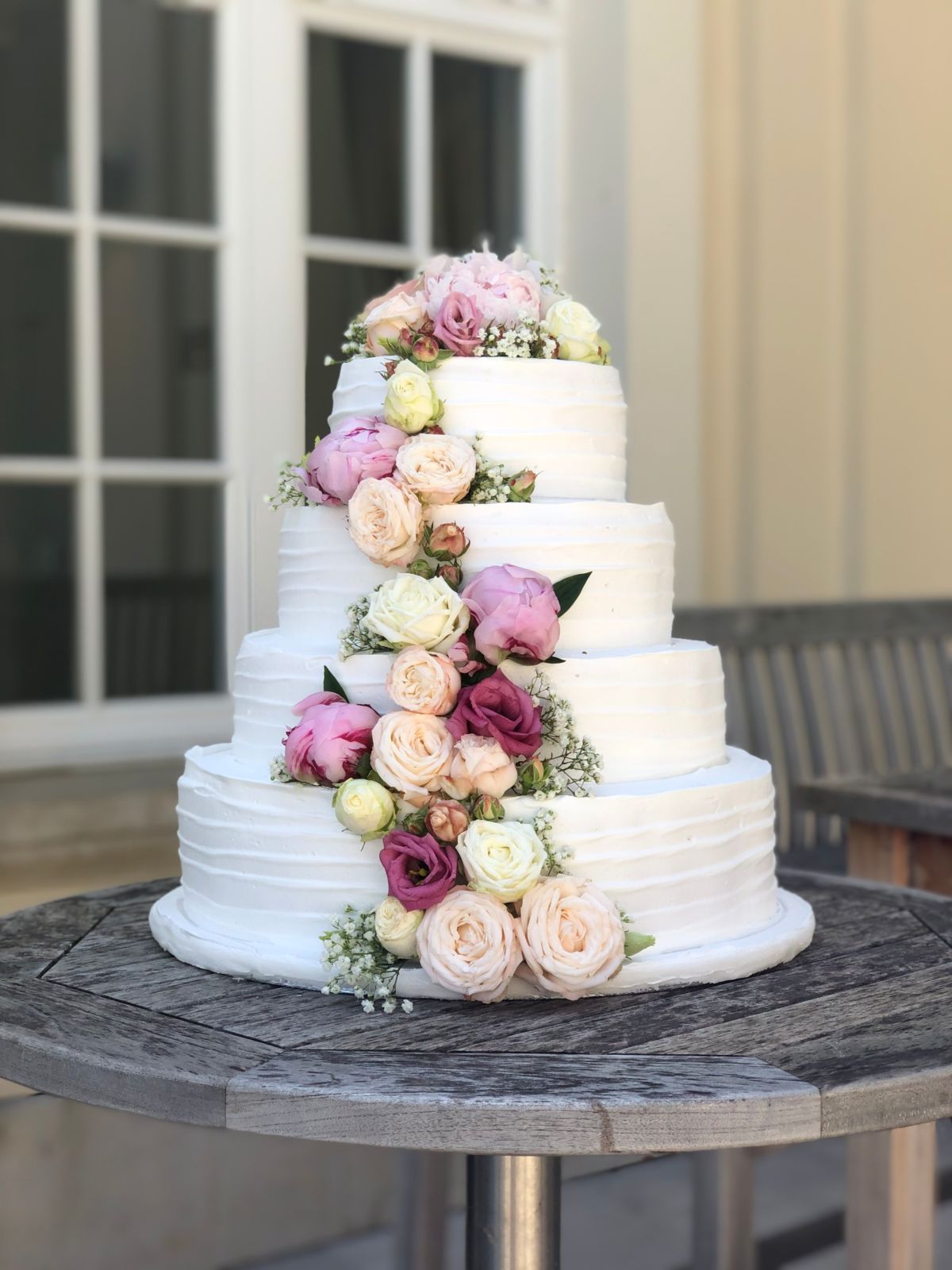 Five-tier wedding cake with cascading mauve, pink and cream roses in outdoor garden setting