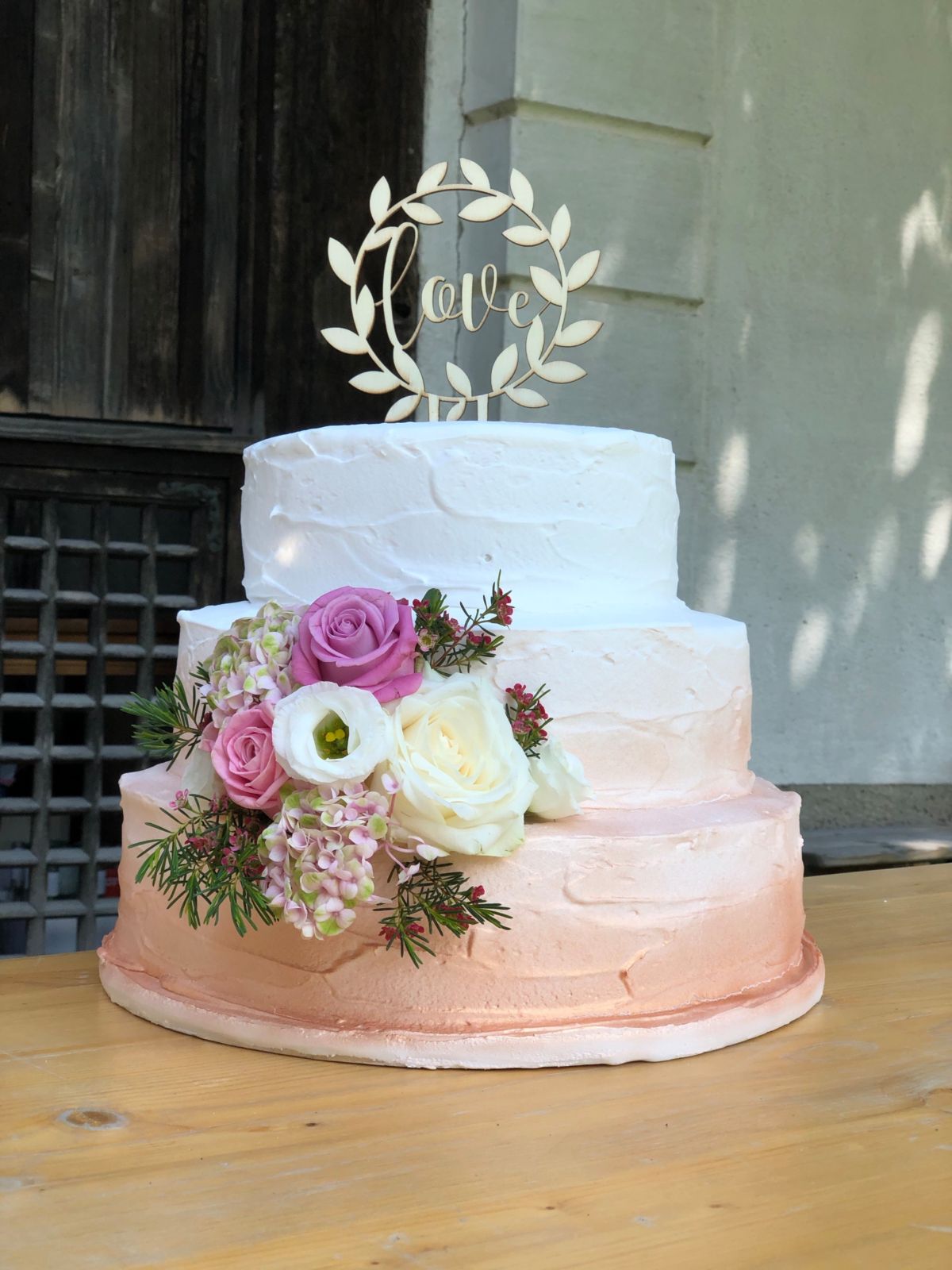 Three-tier ombré wedding cake white to blush with laurel wreath topper and mauve and cream roses