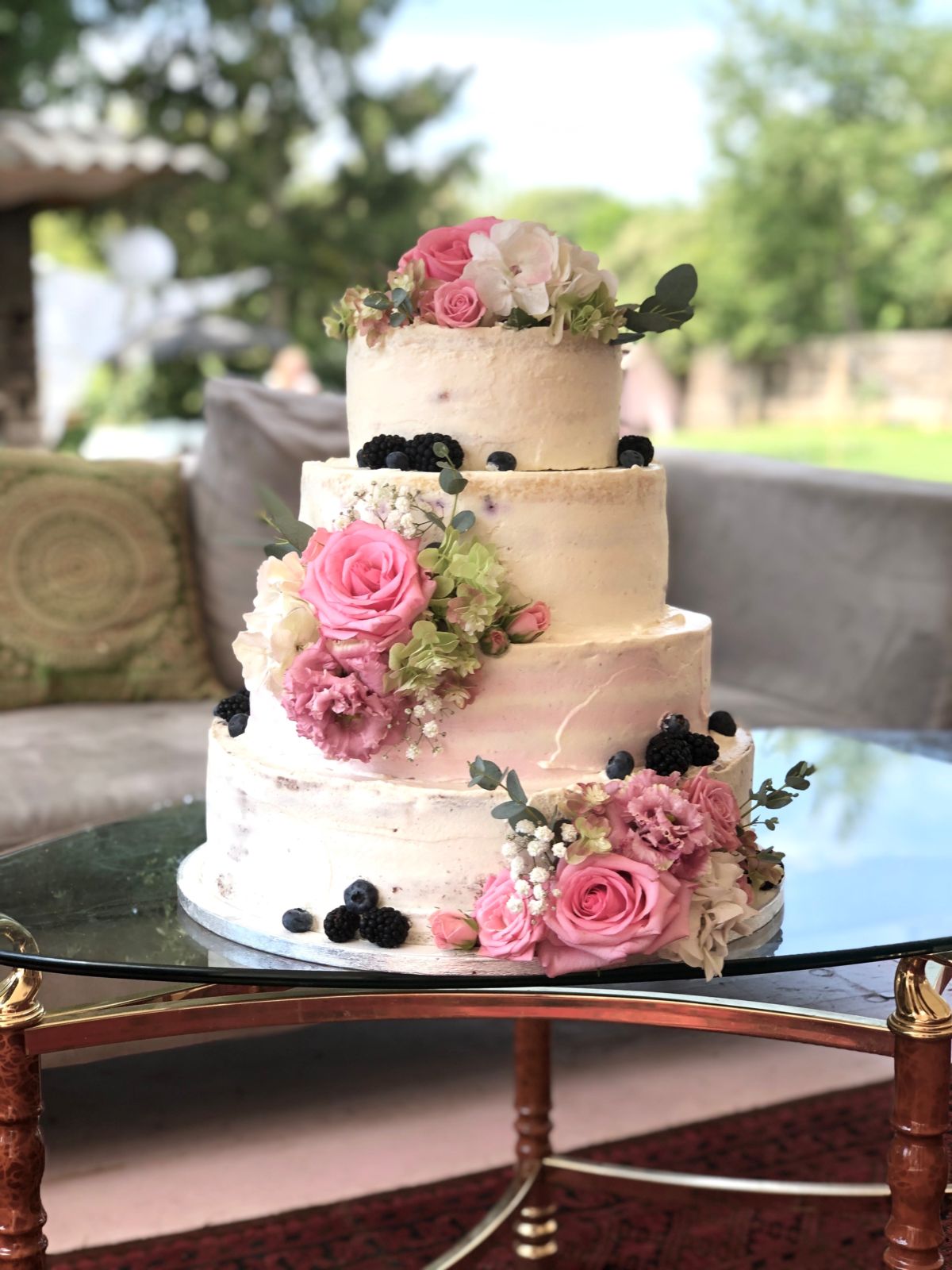 Four-tier wedding cake with pink roses, cream peonies and fresh blackberries in garden setting