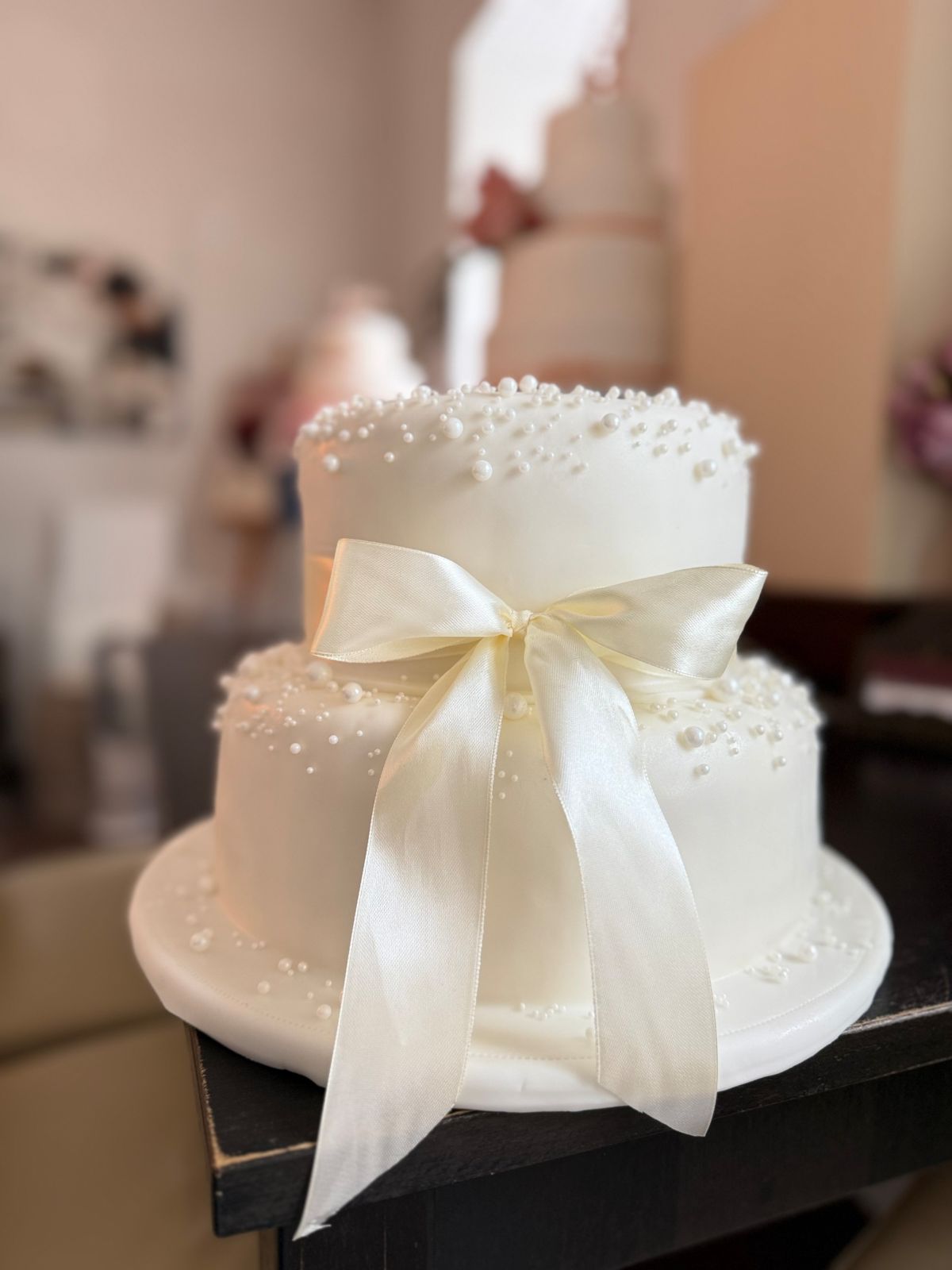 Two-tier white wedding cake with sugar pearls and a large satin bow