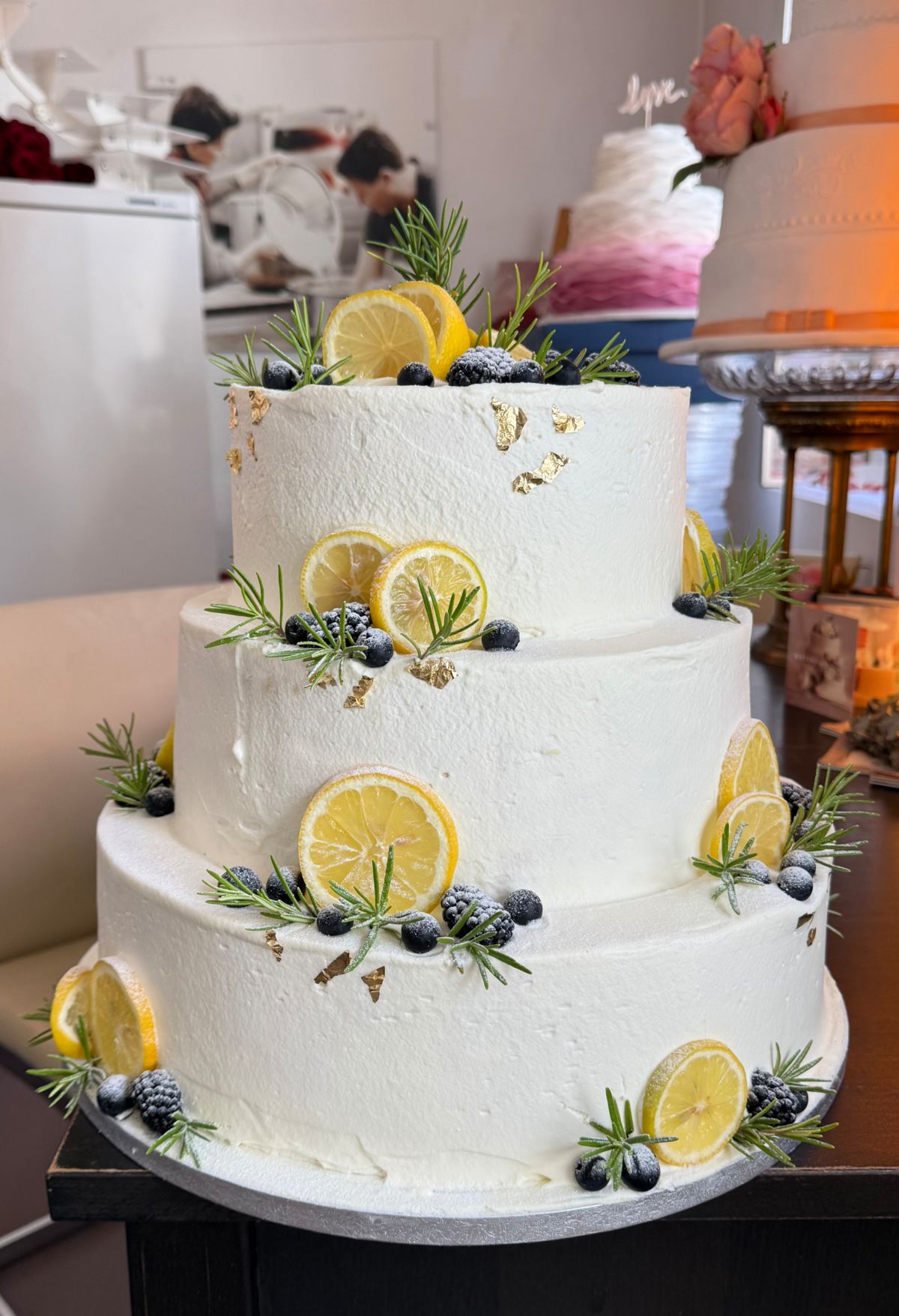 Three-tier wedding cake with lemon slices, blueberries, rosemary and gold leaf