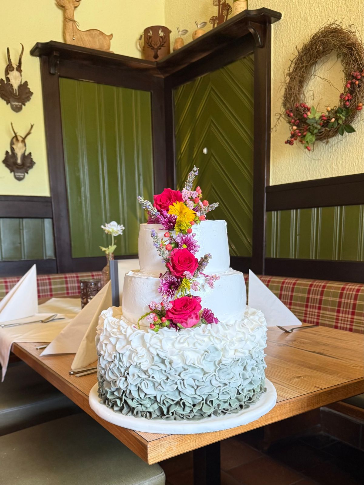 Three-tier wedding cake with mint green ruffles and a cascade of bright flowers