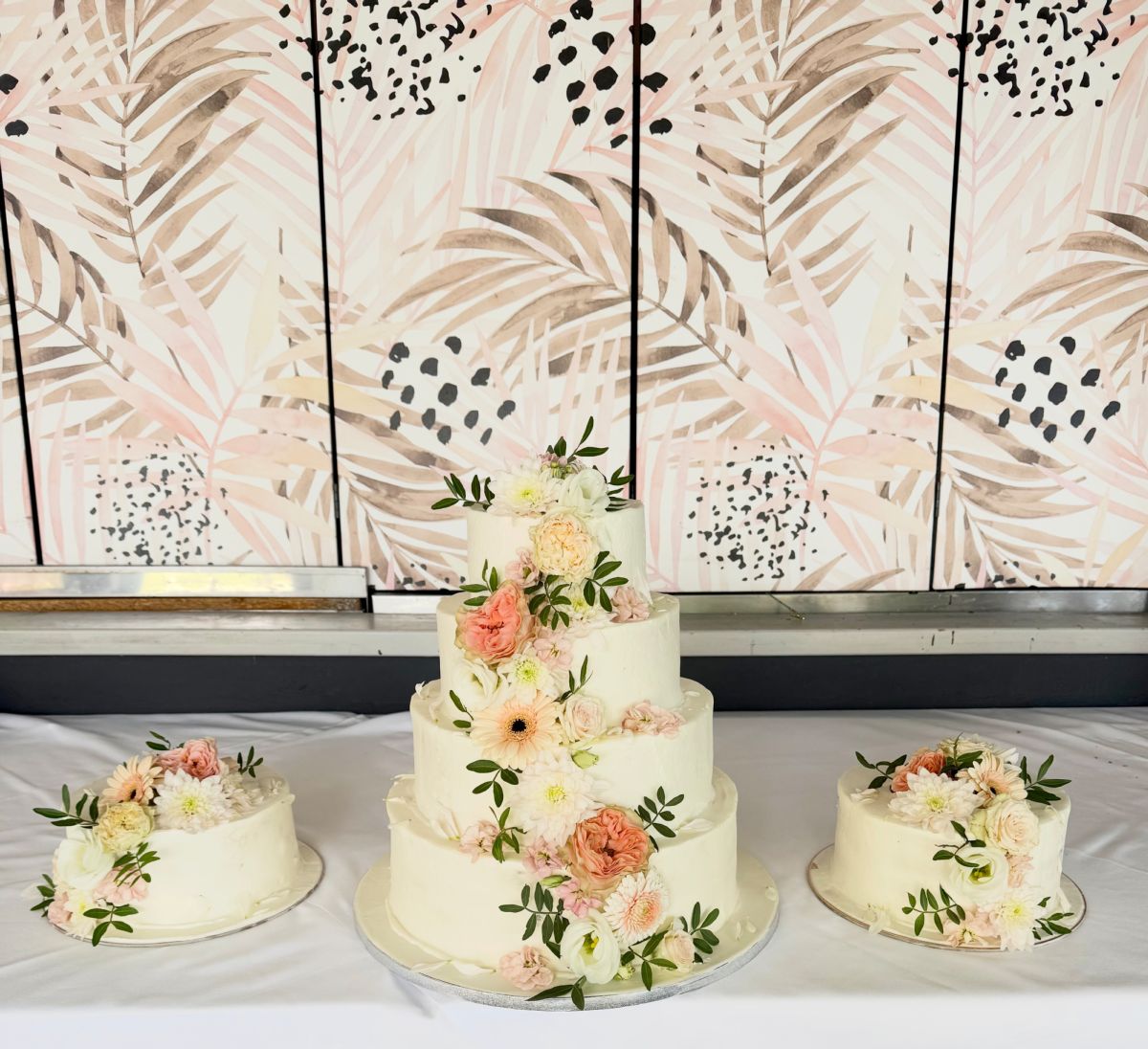 Three-tier wedding cake with peach roses, flanked by two matching single-tier cakes