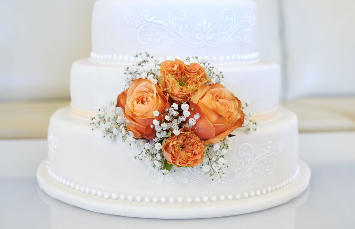 Three-tier white wedding cake with pearl trim and fresh orange garden roses