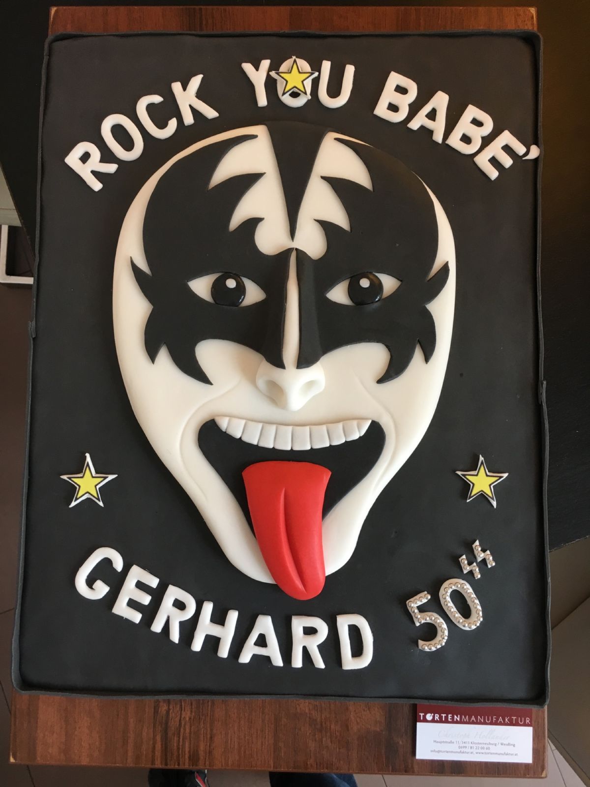 50th birthday cake with rock-inspired black fondant and 3D face with tongue, gold stars
