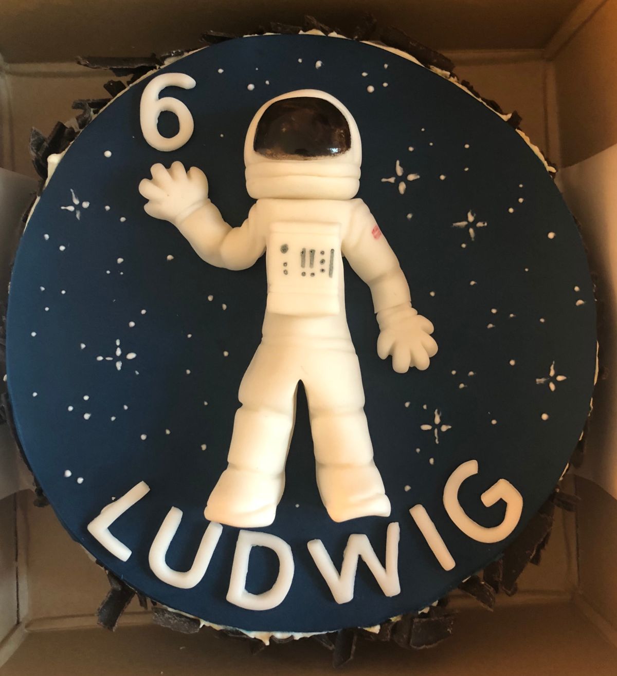 Space-themed children’s birthday cake with white astronaut figure against dark blue starry sky