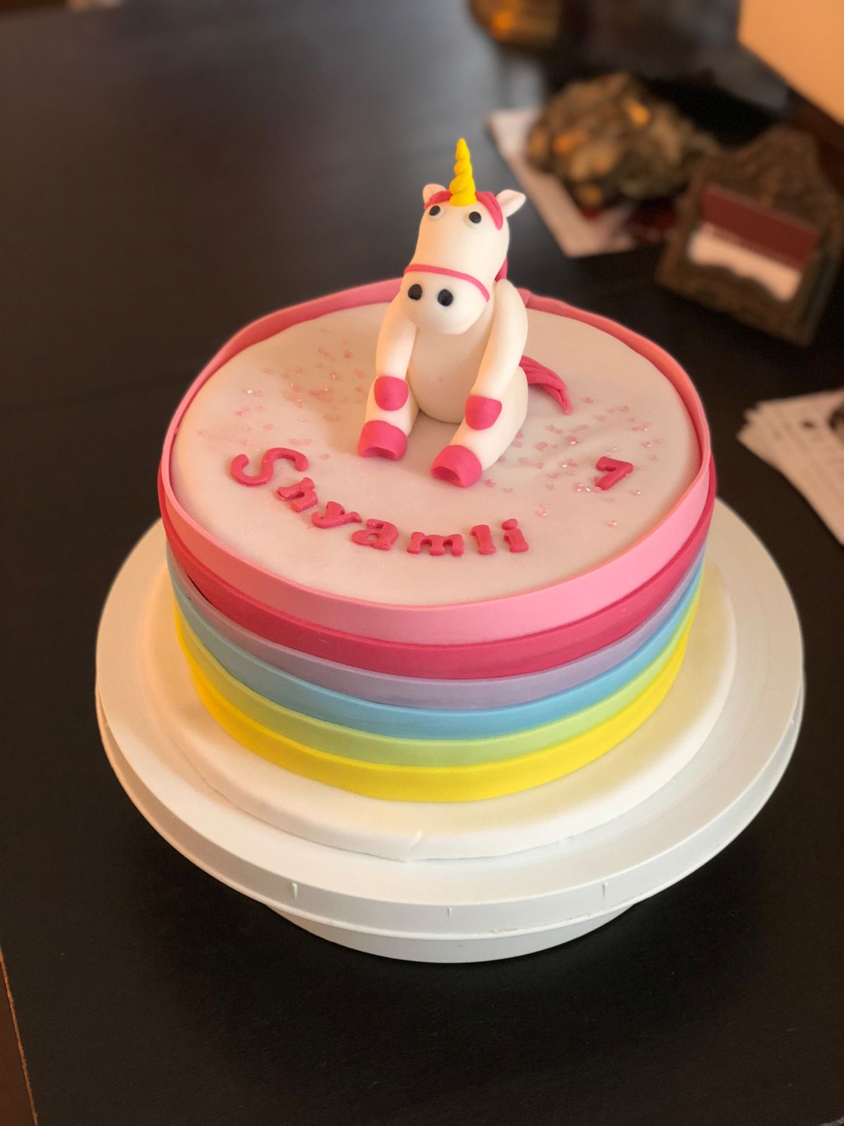 Children’s birthday cake with rainbow-coloured fondant tiers and unicorn toy figurine on top