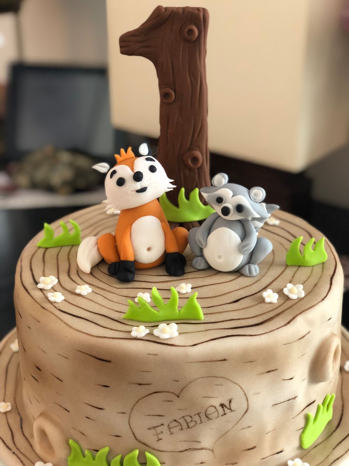 Forest-themed first birthday cake with fondant fox and wild boar figures on buttercream bark texture
