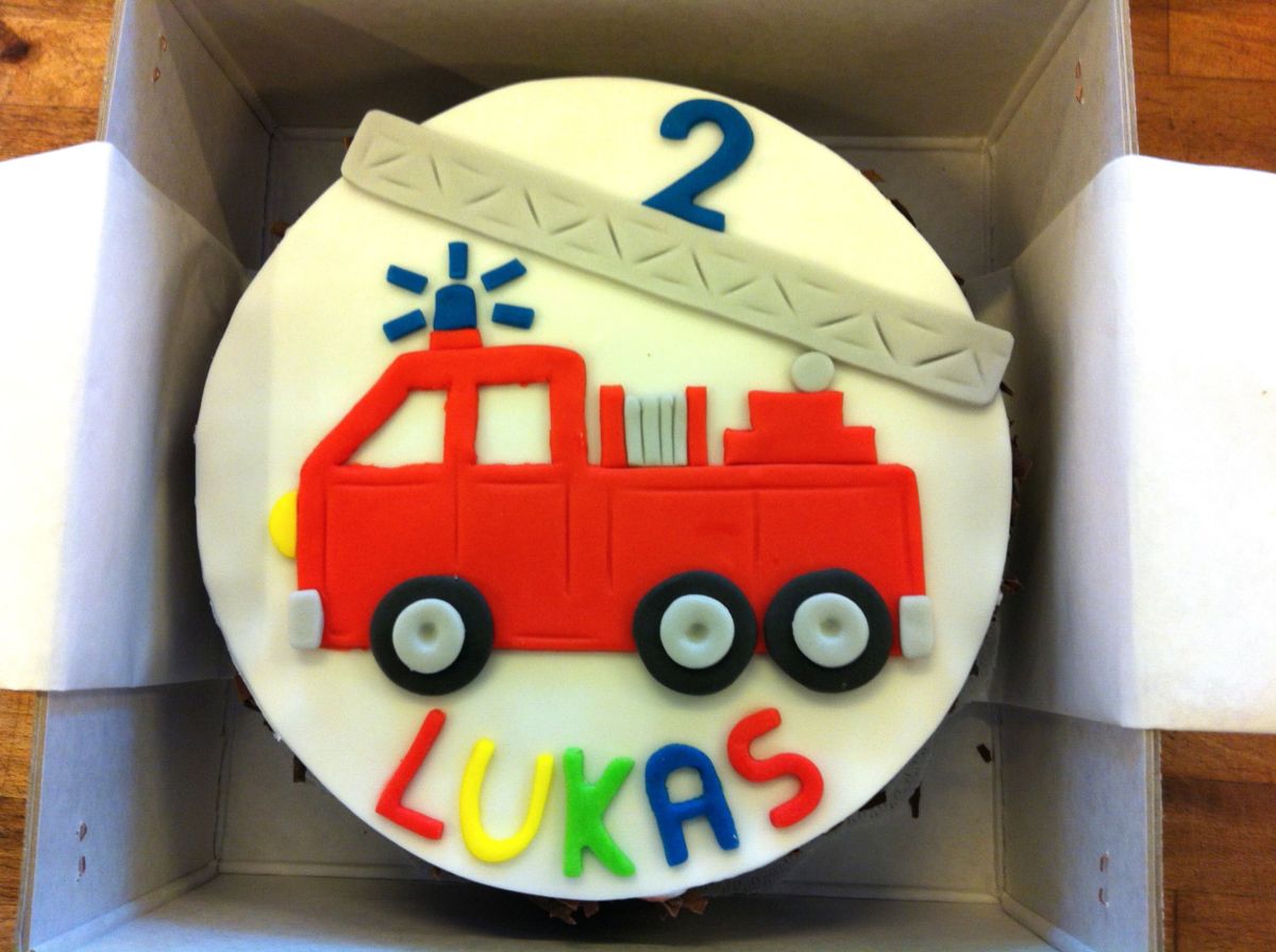 Children’s birthday cake modelled as fire engine with ladder, red and white