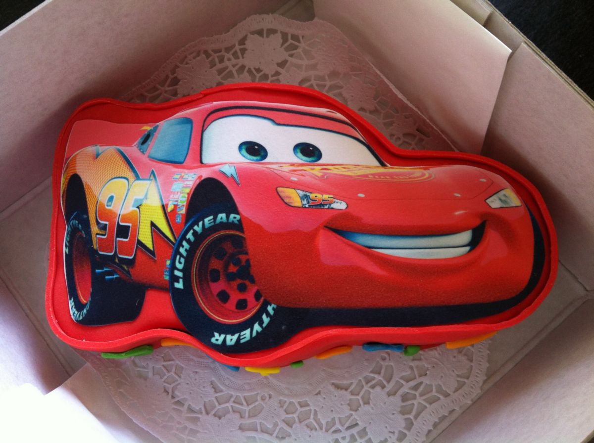Children’s birthday cake shaped and decorated like a red racing car with a large smiling face