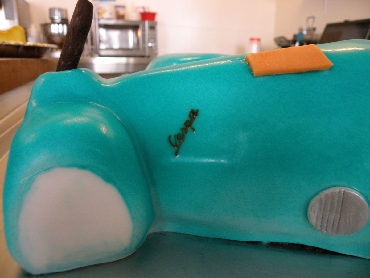 Turquoise Vespa scooter cake with orange seat and detailed white tyres
